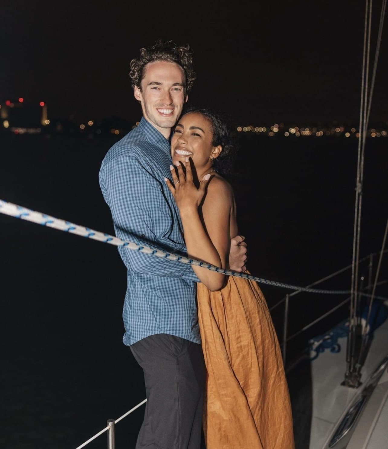 A couple embracing on deck with San Diego city lights across the water on a winter sail