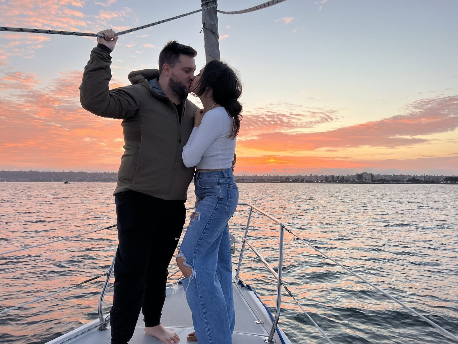 A couple kissing on the bow at sunset during a proposal cruise on San Diego Bay