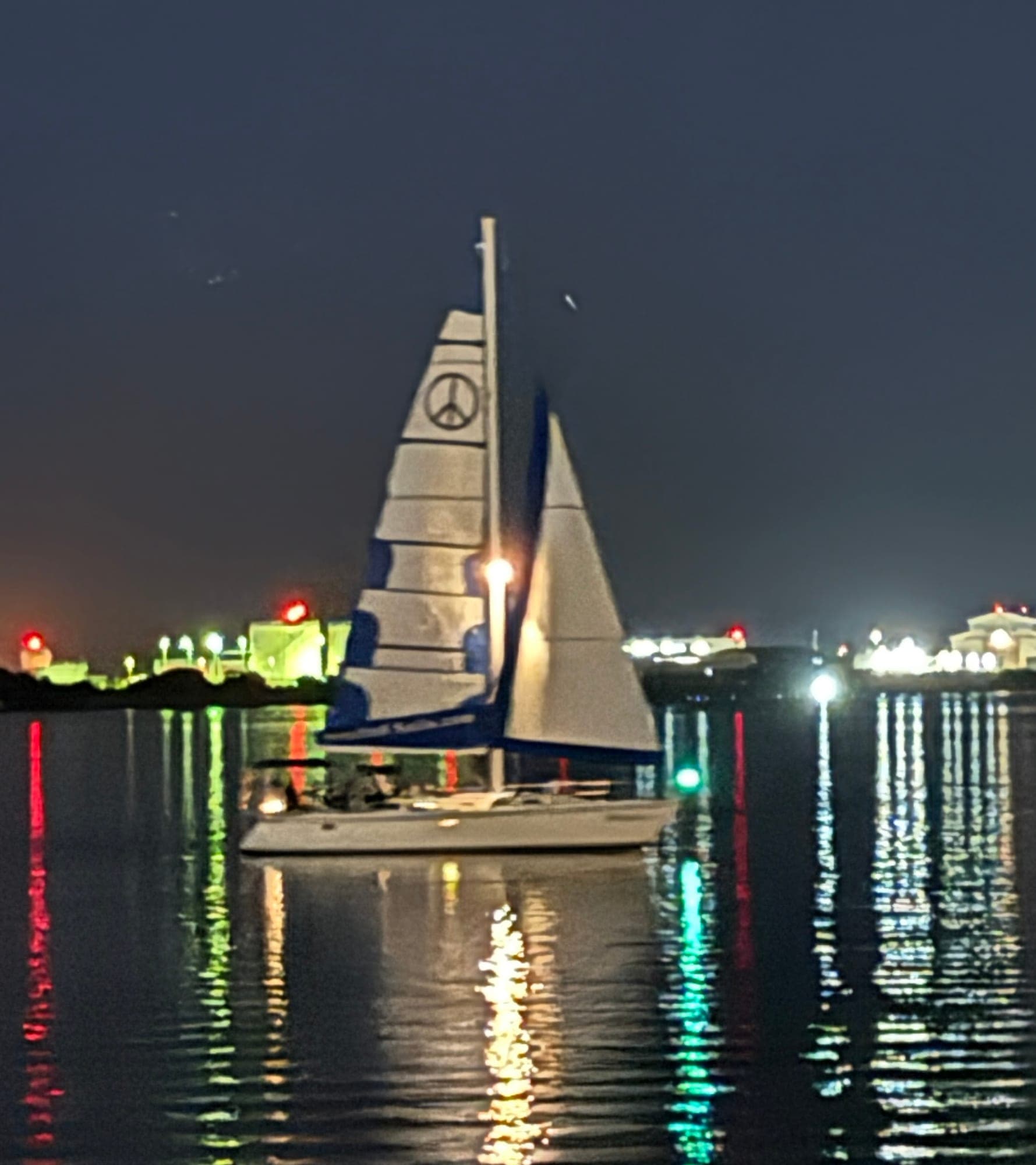 The Mojave under her peace-sign mainsail at night, harbour lights reflected across San Diego Bay